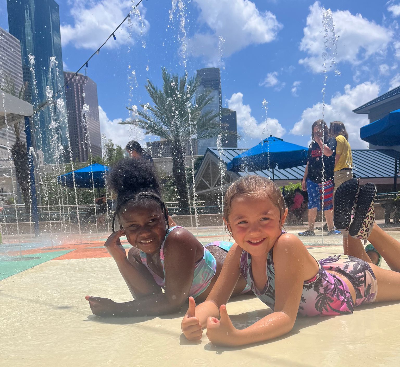 Two little girls are laying on the ground giving a thumbs up