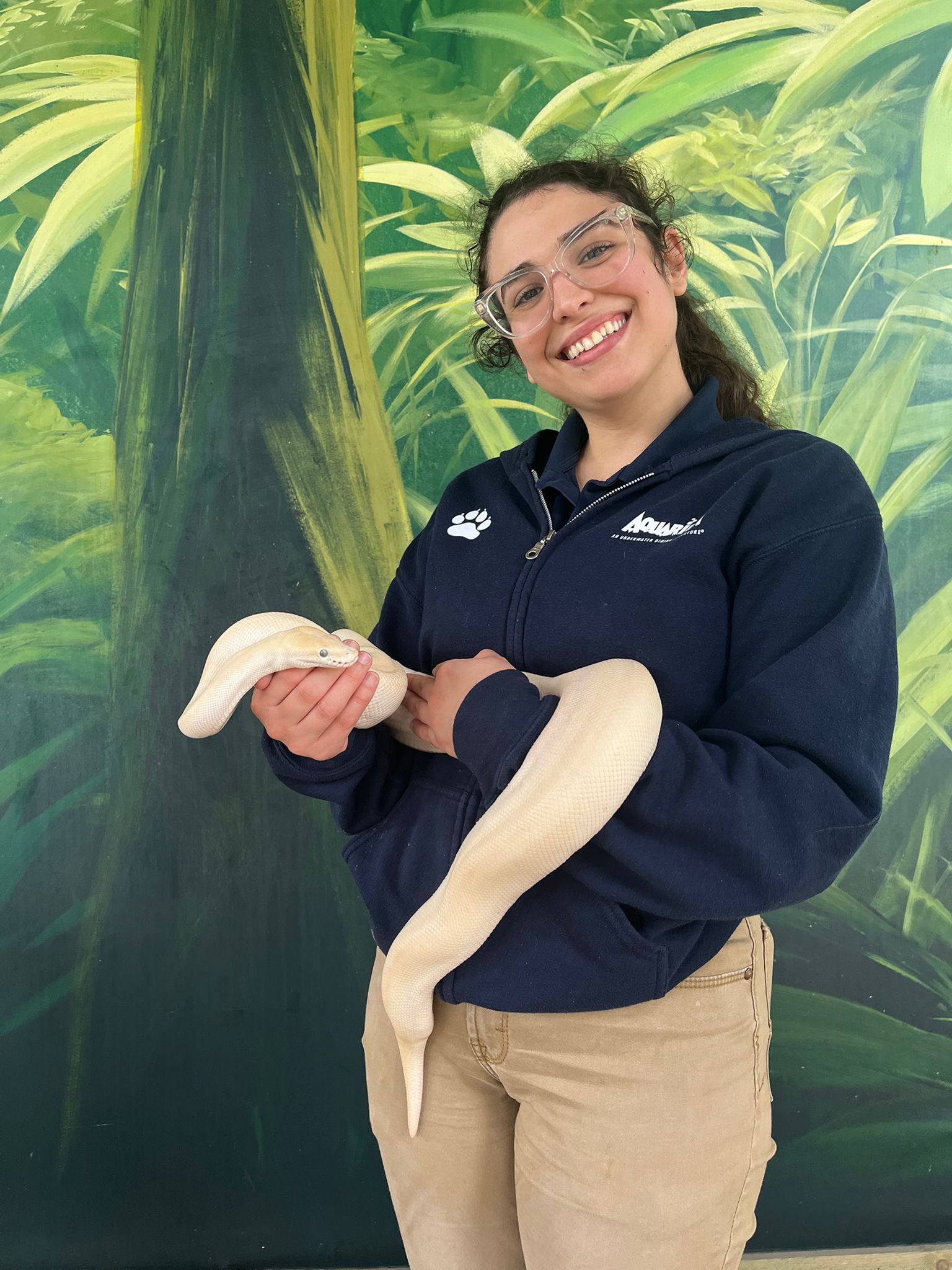 A woman in a blue jacket is holding a white snake
