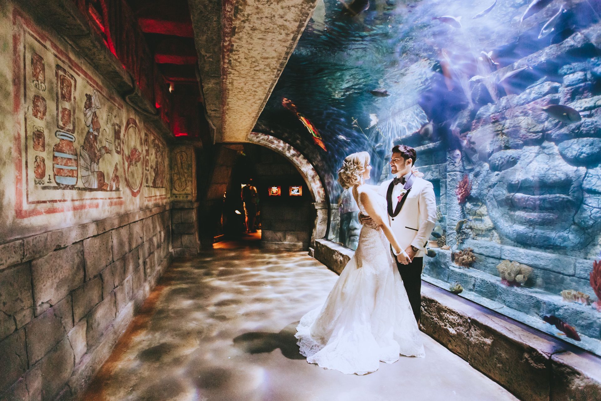 A bride and groom holding hands in front of an aquarium