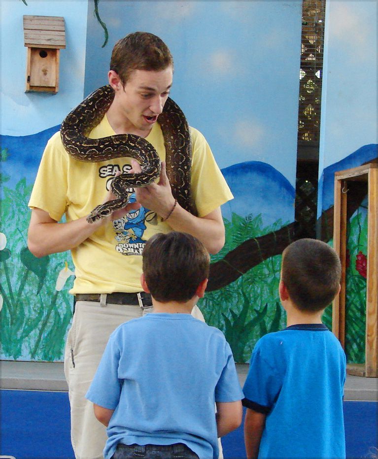 A man holding a snake showing two children