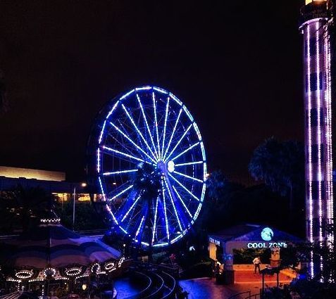 A ferris wheel is lit up at night in color blue at an amusement park