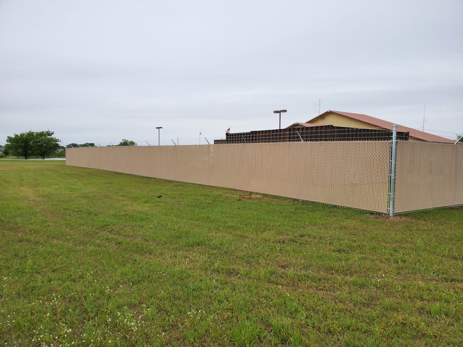 A long fence surrounds a grassy field with a building in the background.