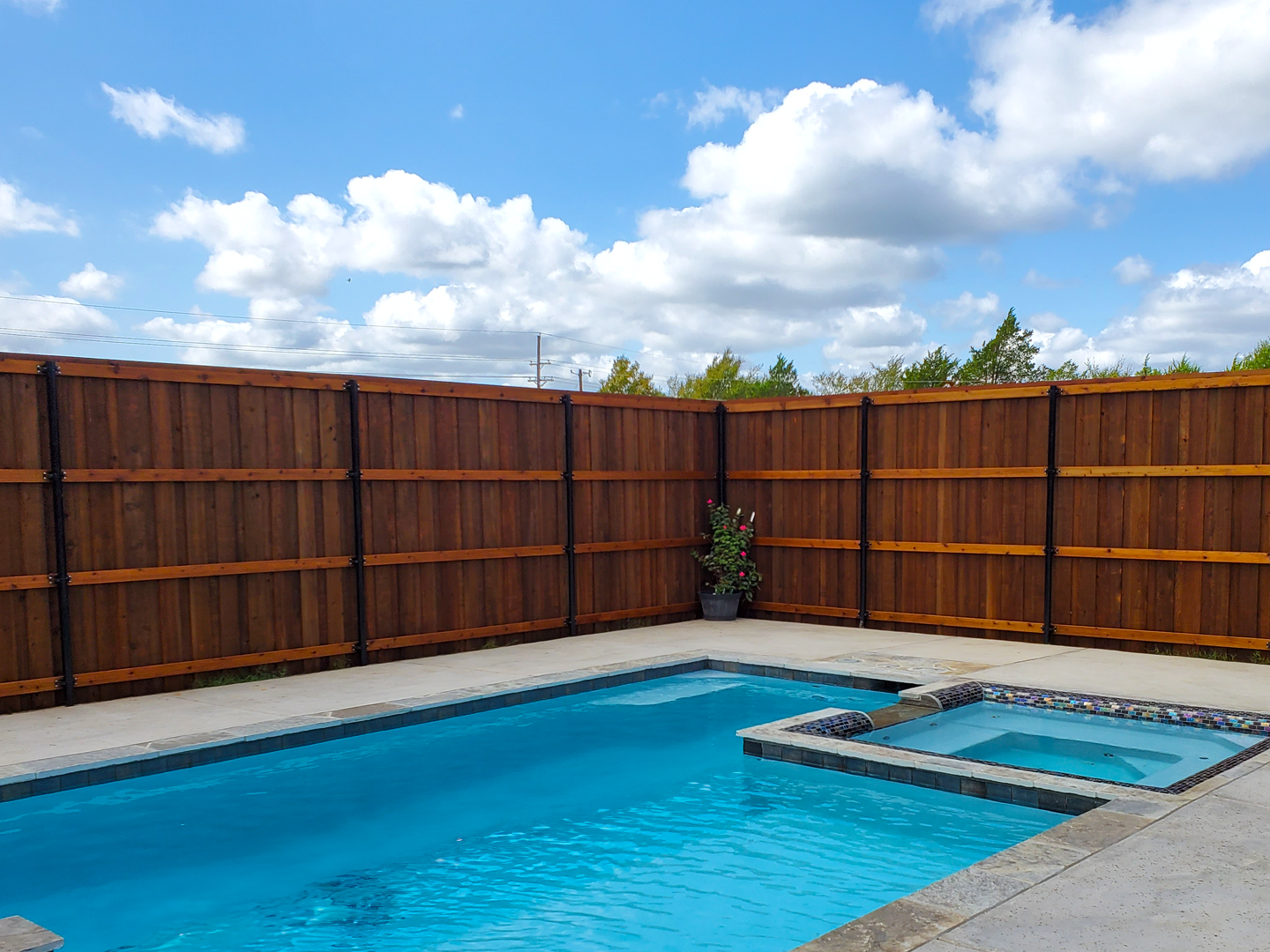 A large swimming pool surrounded by a wooden fence on a sunny day.