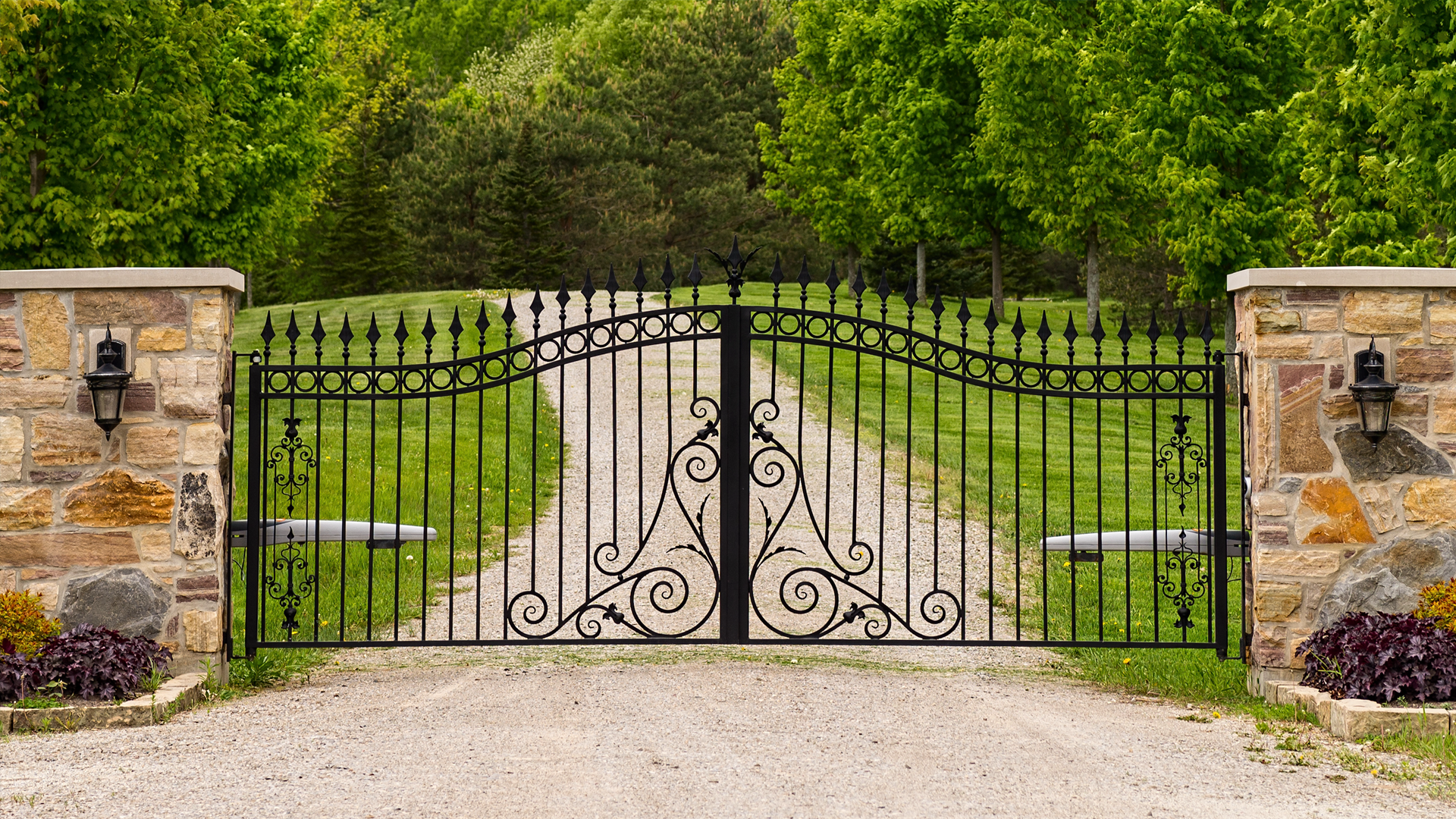 A wrought iron gate is leading to a gravel driveway.