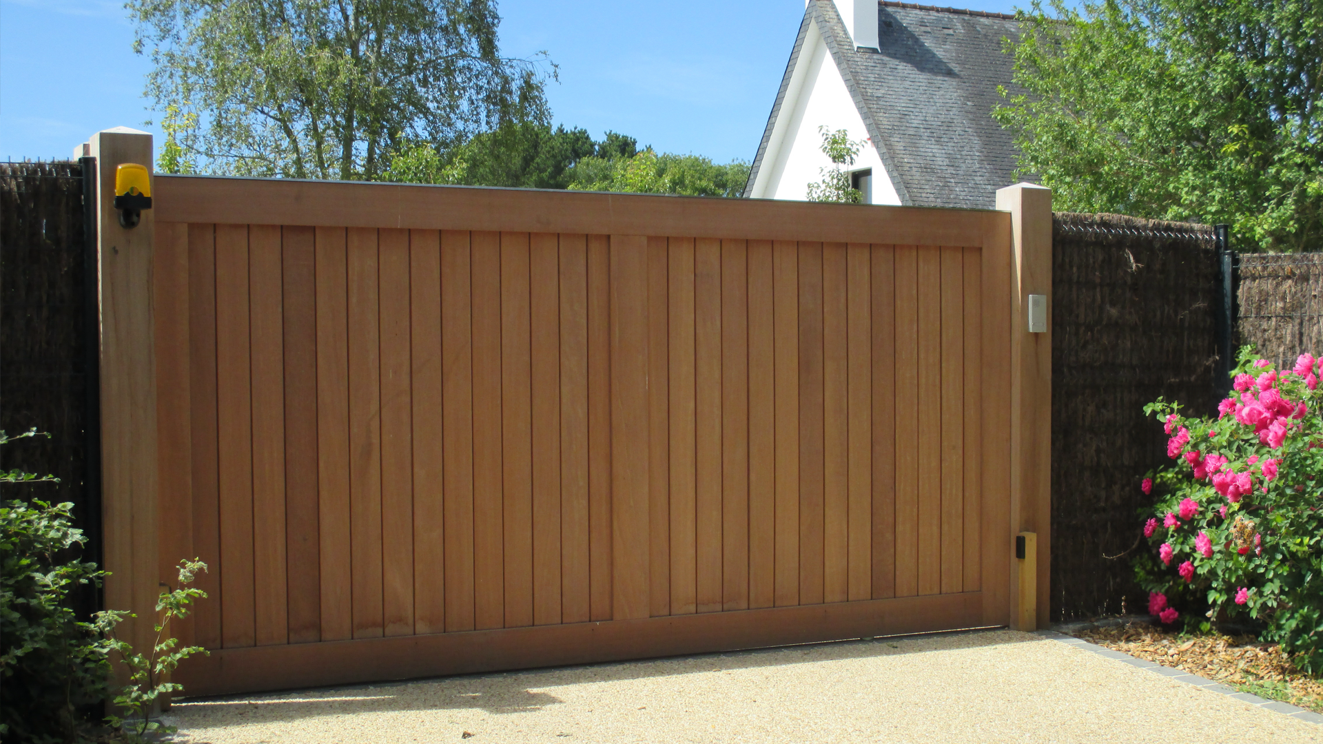 A wooden gate is open to a driveway in front of a house.