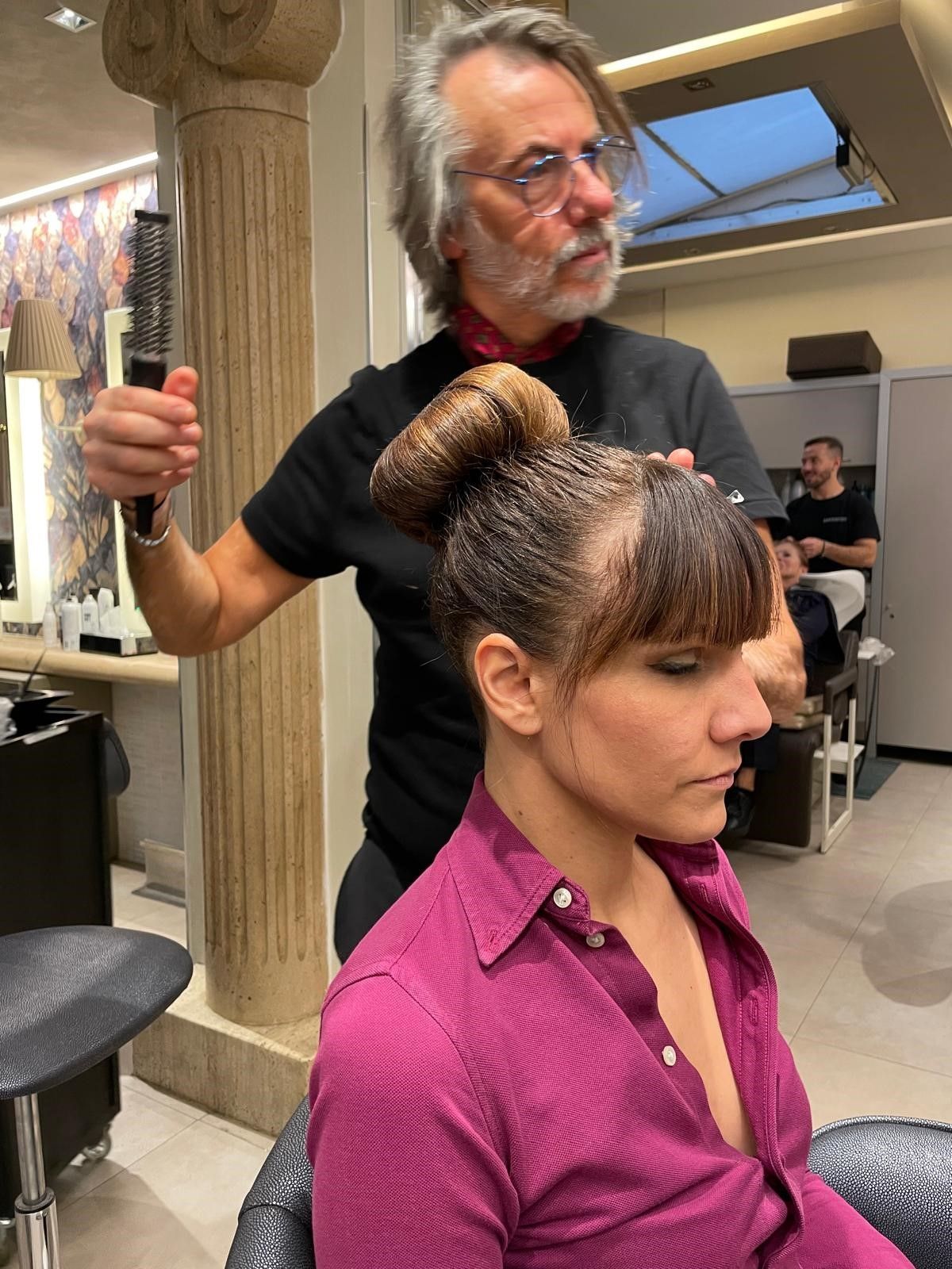 Una parrucchiera usa una spazzola per dare forma ai capelli di una cliente seduta sulla poltrona del salone.