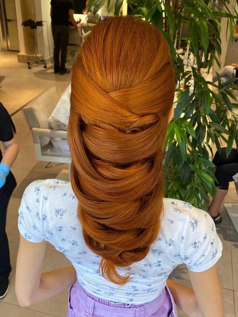Una persona con lunghi capelli color rame brillante, acconciati in una coda di cavallo voluminosa e ondulata, in un salone di bellezza.