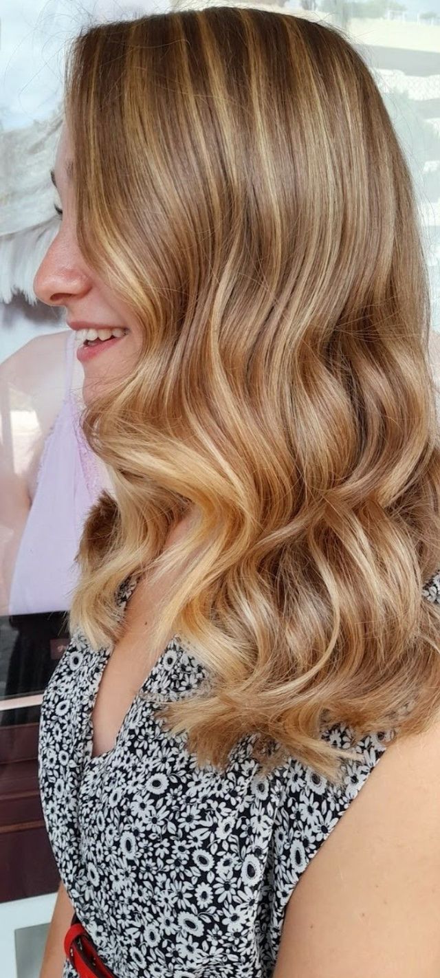 Vista di profilo di una persona con lunghi capelli mossi color castano dorato che indossa una maglietta a fantasia bianca e nera.
