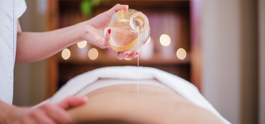 In un ambiente rilassante e a luci soffuse, una massaggiatrice versa dell'olio da massaggio sulla schiena di una persona.