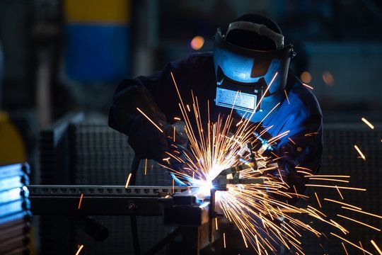 Welder in a workshop using a welding torch, with sparks flying.