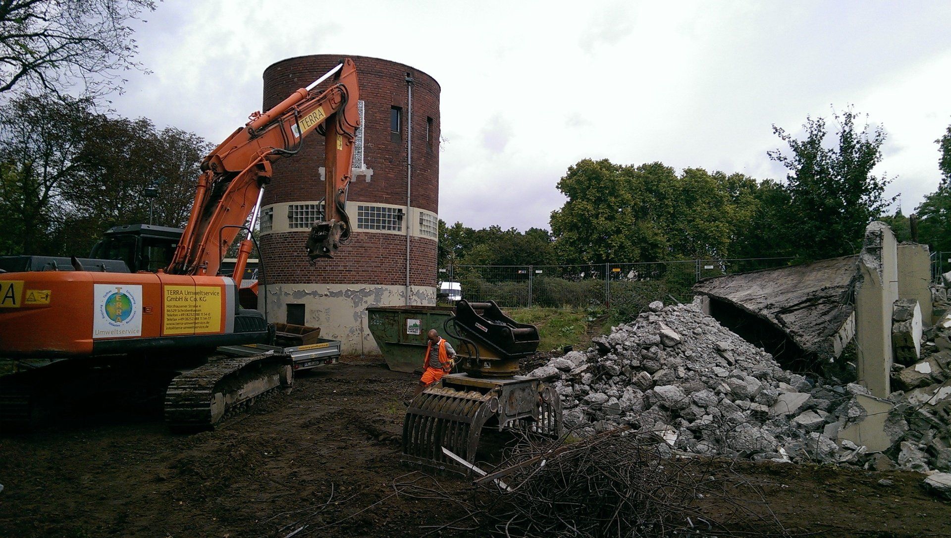 Ein großer Bagger zerstört ein Gebäude auf einem Feld.