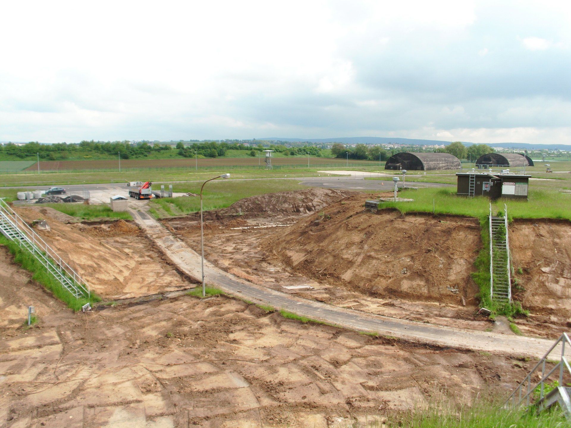 Ein Feldweg führt durch ein Feld, im Hintergrund ist ein Gebäude zu sehen.