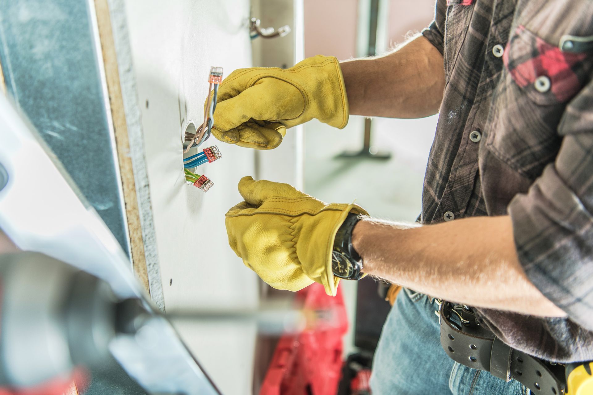 Male residential electrician with a safety hat and yellow gloves installs an outlet on a building’s wall.
