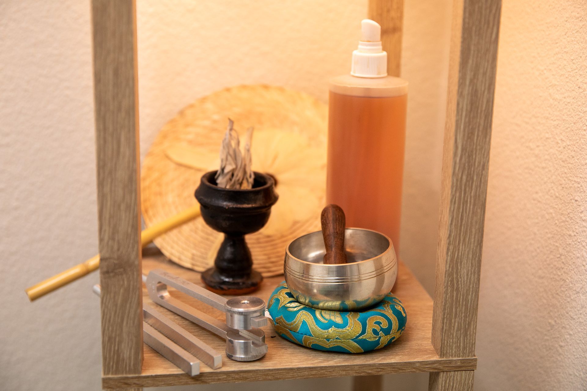 Shelf with a singing bowl, incense, fan, bottle, and tuning forks.