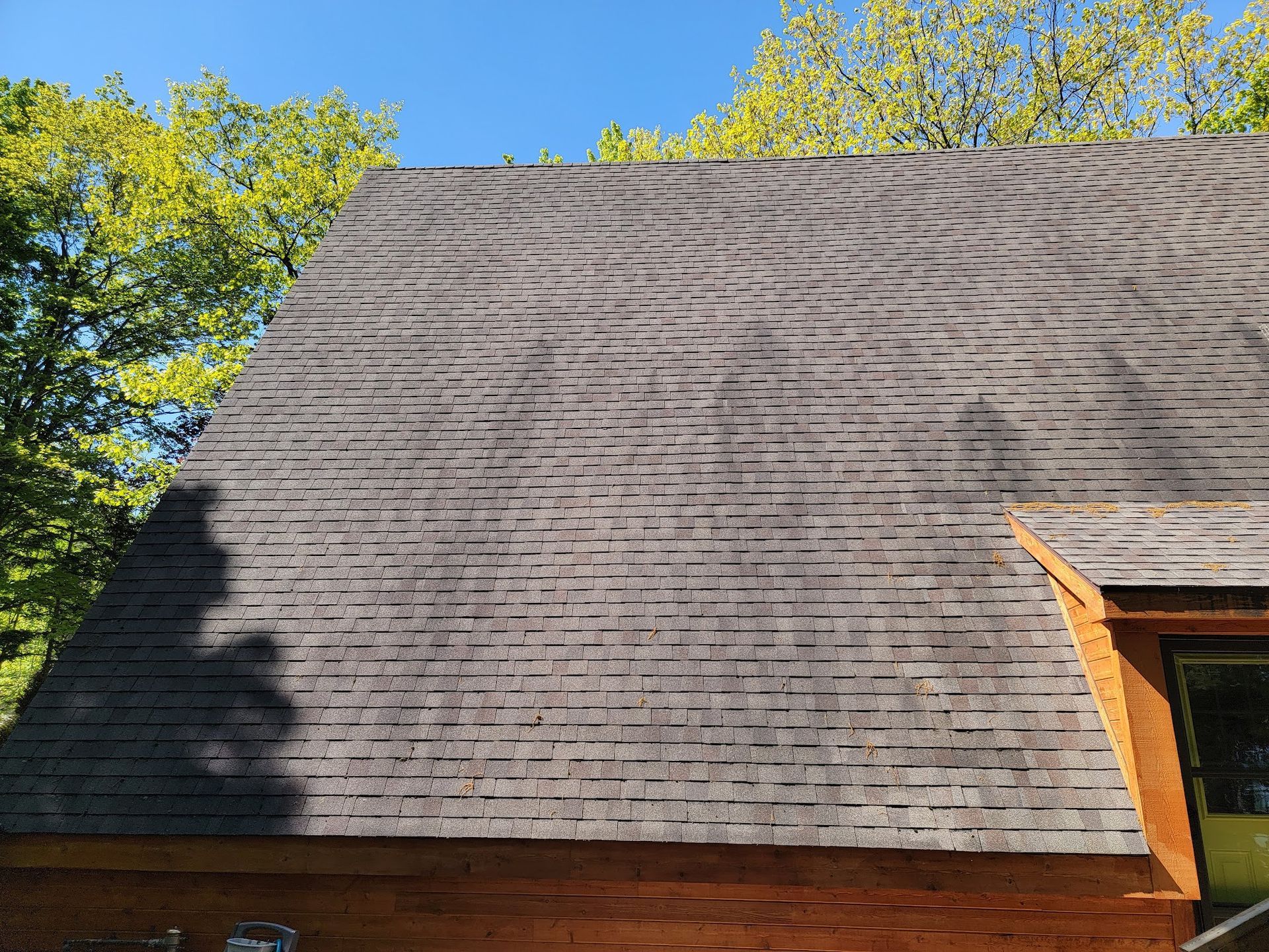 Shingled roof of a cabin with curved dark streaks, possibly from the sun or weather damage.