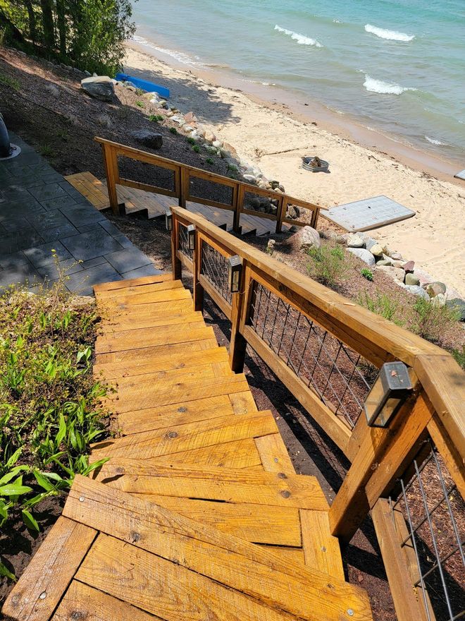 Wooden stairs leading down to a sandy beach with a turquoise ocean. The stairs have a railing.