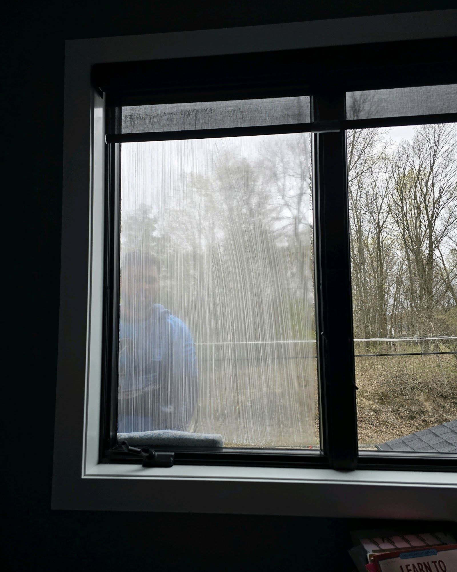 Window being cleaned, streaks visible. A person in blue shirt is visible in the reflection.