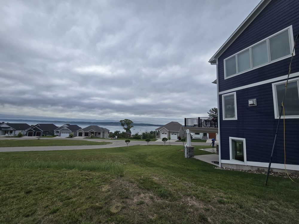 A dark blue house with white trim overlooks a lake and cloudy sky.