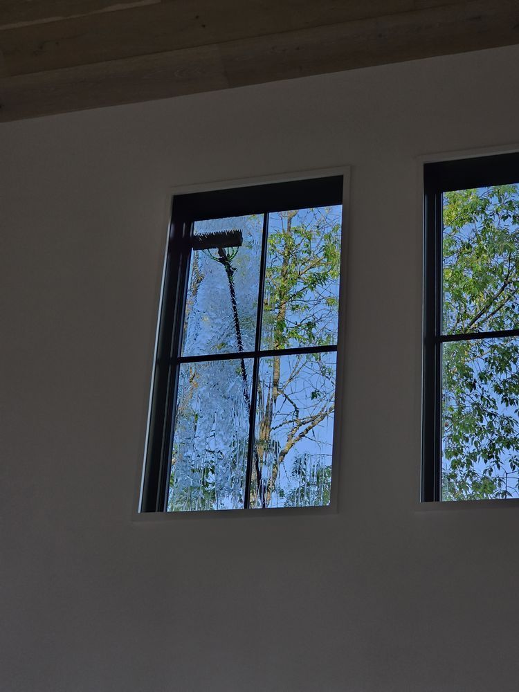 Two rectangular windows with black frames on a white wall. Through the left window, a person is cleaning .