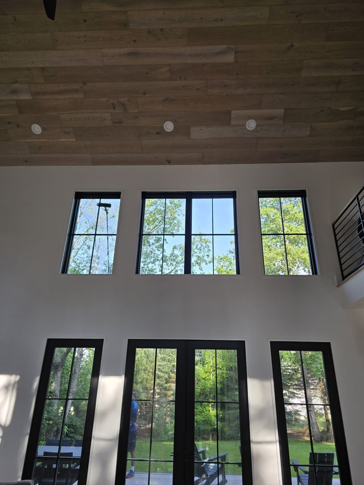 Interior view of a room with three tall windows above three door-like windows. Bright white walls and a wood plank ceiling.