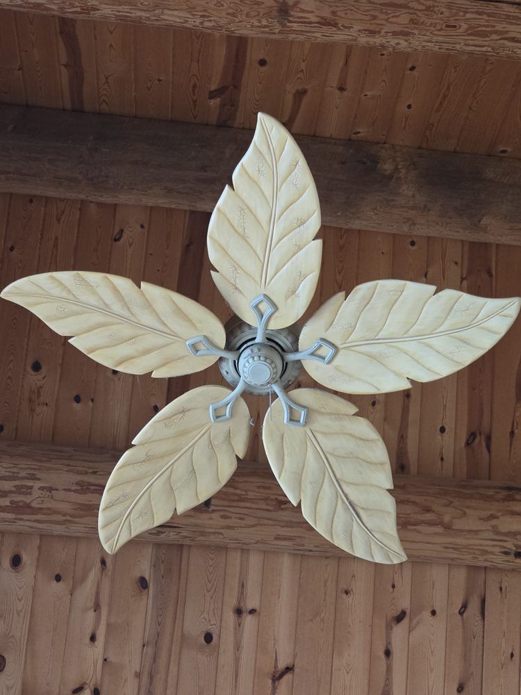 Ceiling fan with five leaf-shaped blades, light wood against a wooden ceiling.