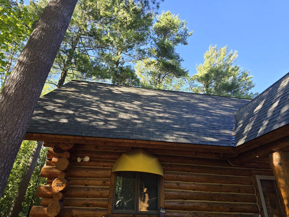 Log cabin with a dark shingled roof, a golden dome, and green trees against a blue sky.