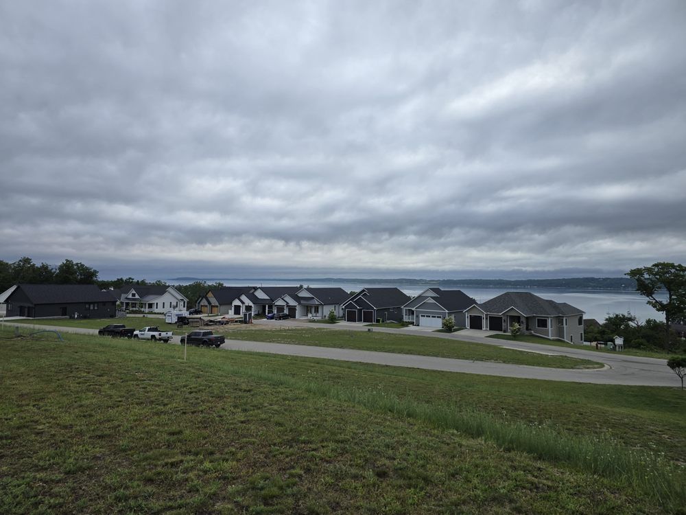 Row of modern houses on a grassy hill overlooking a body of water under a cloudy sky.