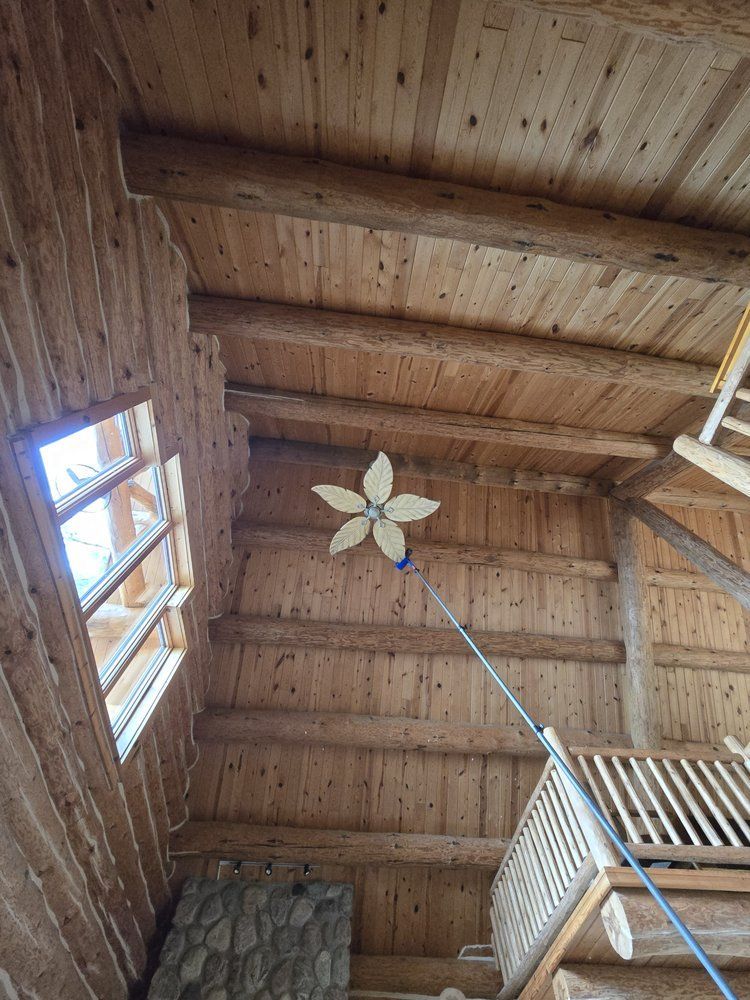 Interior view of a rustic cabin with exposed wooden beams. A large wooden flower hangs from the ceiling.