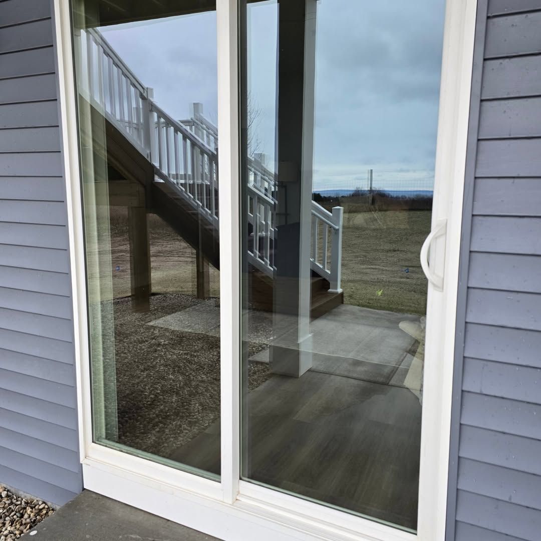 Sliding glass door with white frame reflecting outdoor stairs, a concrete patio, and a distant field under a cloudy sky.