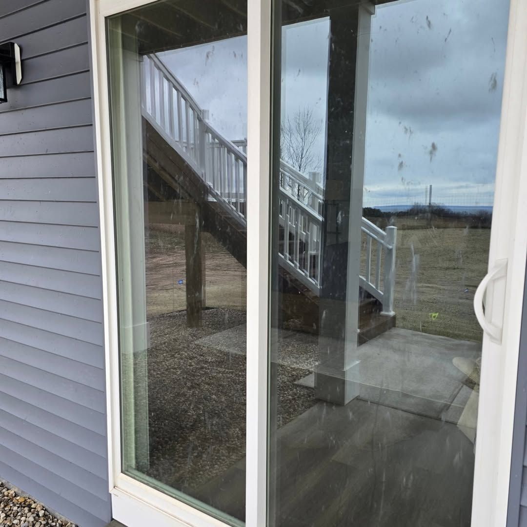 Sliding glass door reflecting a wooden staircase, cloudy sky, and gray siding. White door frame and handle.