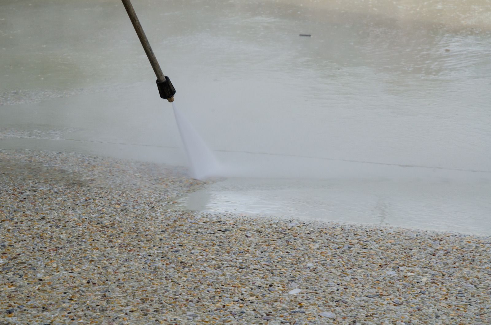 A pressure washer cleaning a speckled concrete surface, leaving a clean, wet path.