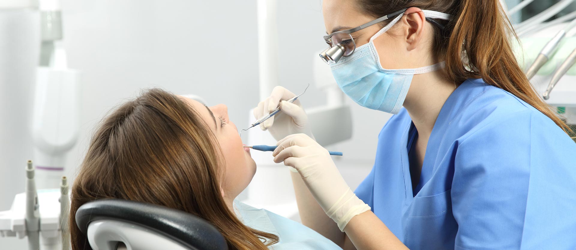 A woman is sitting in a dental chair while a dentist examines her teeth.