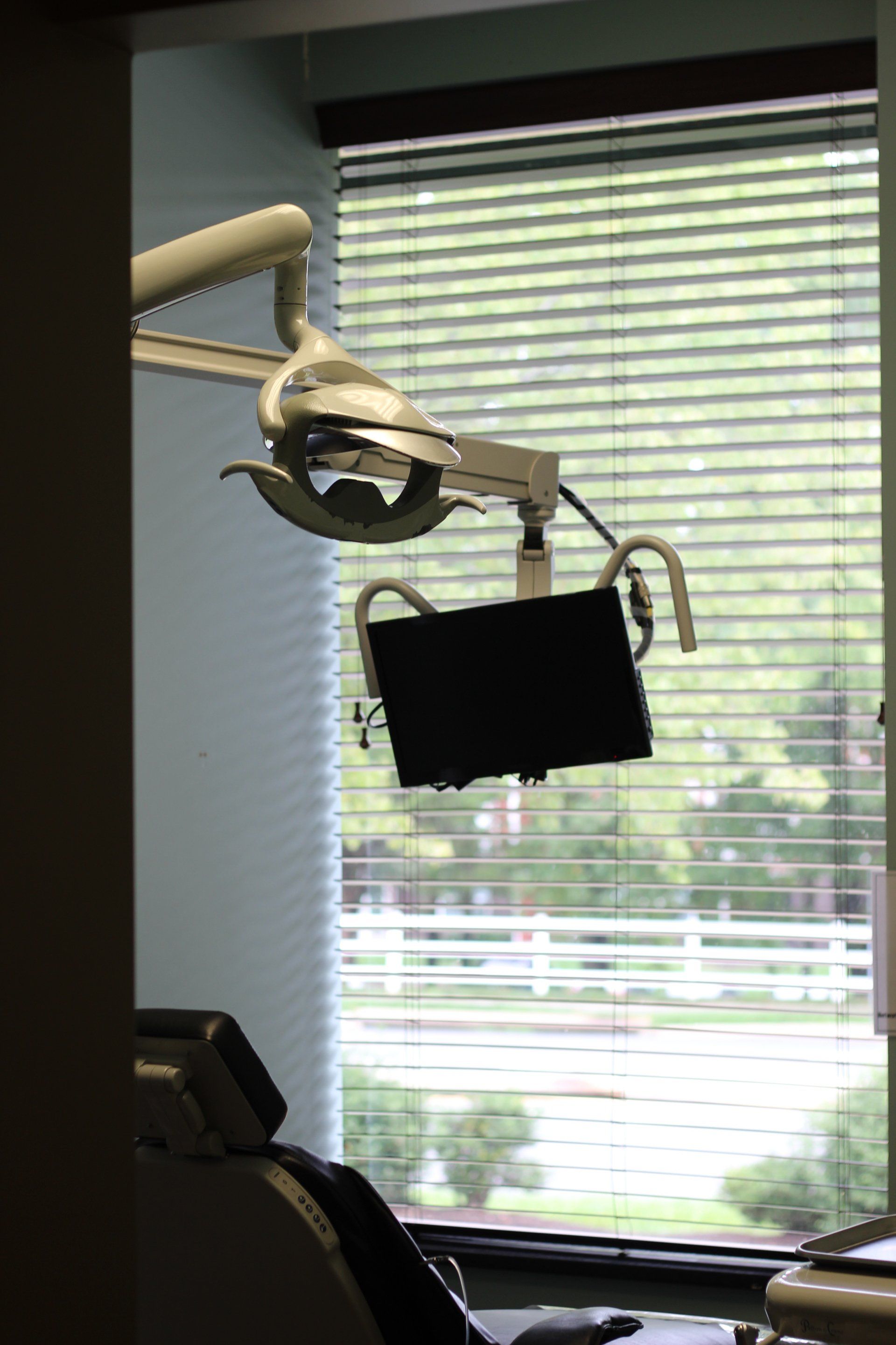 A dental office with a dental chair and a monitor hanging from the ceiling.