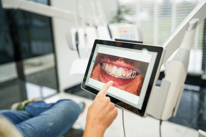 Person points at digital image of teeth with dental appliance on tablet in dental office.