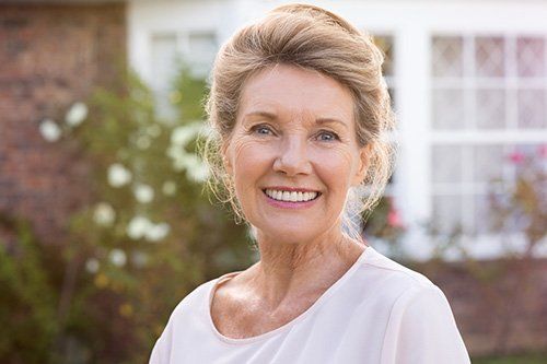 An older woman is smiling in front of a house.