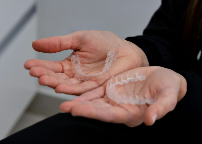 Hands holding upper and lower clear dental aligners.