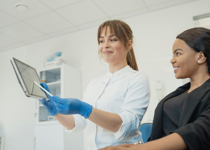 Dentist shows patient X-ray on tablet in a brightly lit office. The patient is smiling.