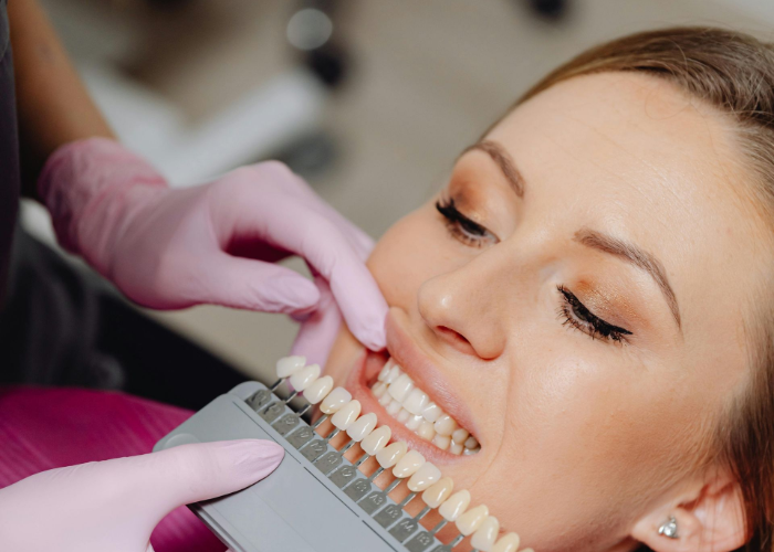 Dentist matching teeth shade with a color guide on a patient in a dental office.
