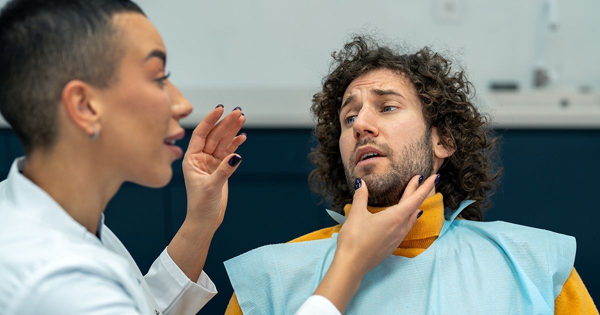 A woman is talking to a man in a dental chair.