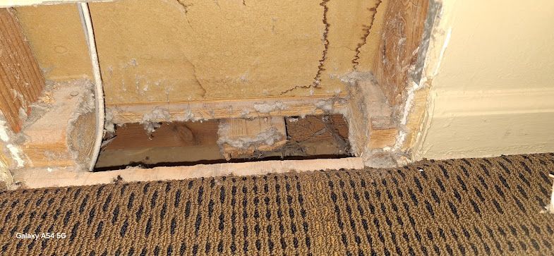 A hole in a wall next to a carpet in a room.