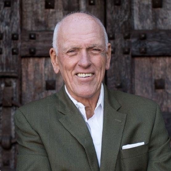 Man in green blazer smiles, white pocket square, against a wooden door.