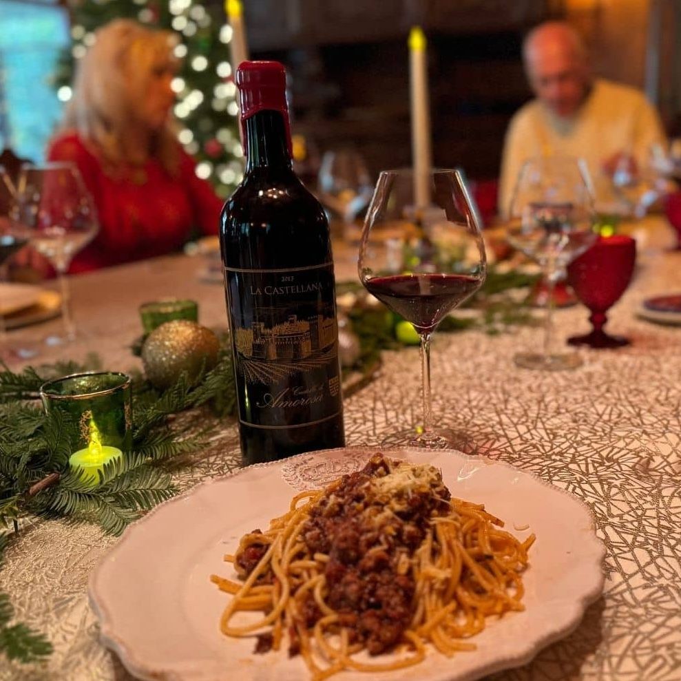 Spaghetti dinner with wine bottle, filled glass, and people seated at a table decorated for the holidays.
