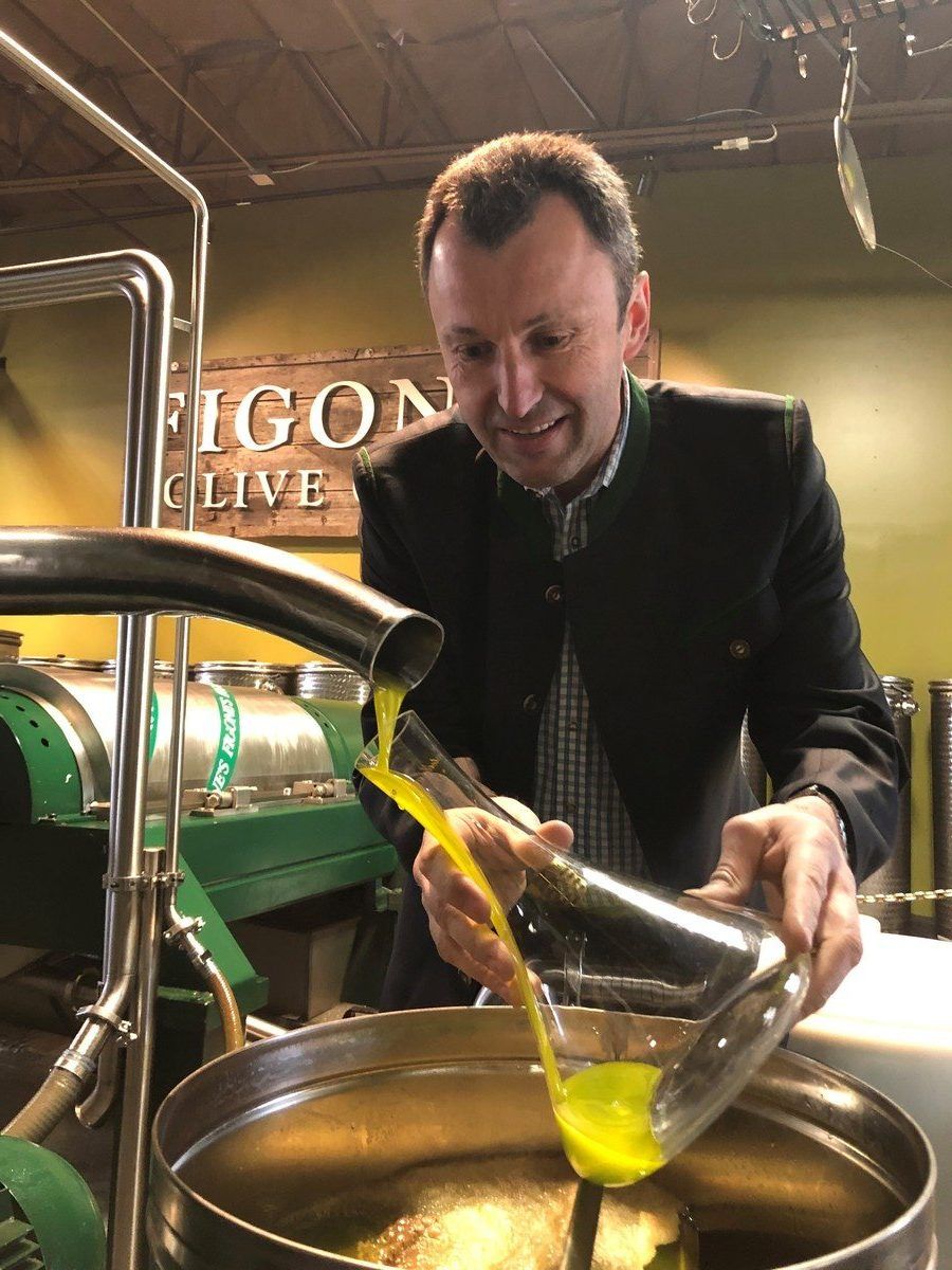 Man pouring olive oil into a glass container in a production facility.