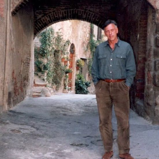 Man in green shirt and brown pants stands in arched walkway.