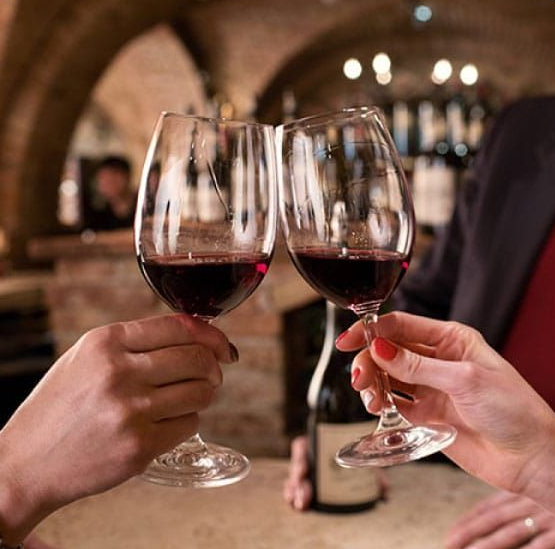 Two hands clinking wine glasses filled with red wine. In a wine cellar setting.