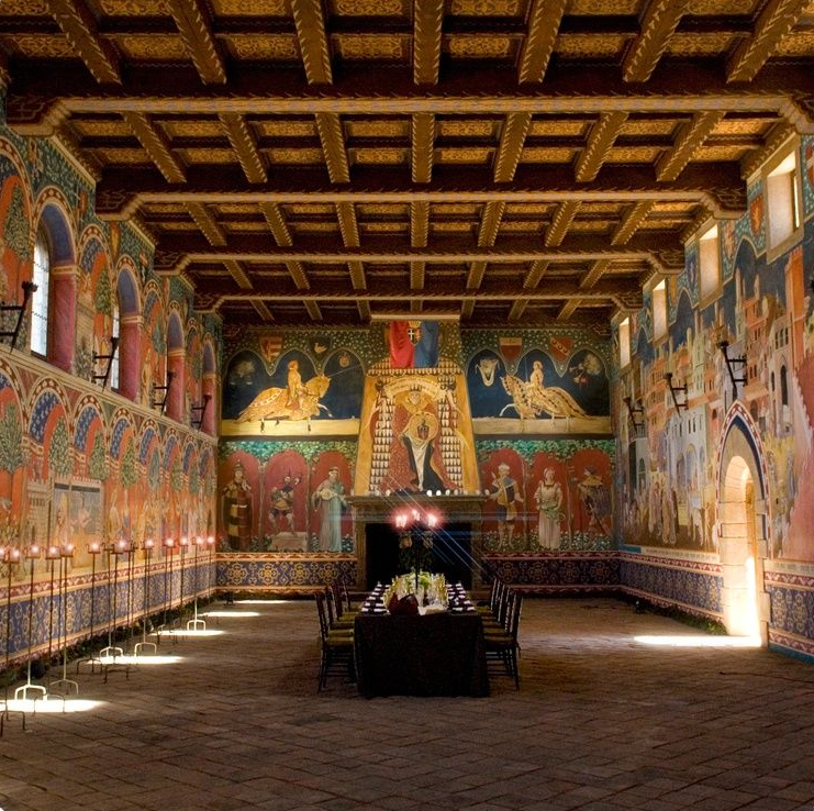 Grand dining hall with ornate painted walls, wooden ceiling, and long table set for a meal.