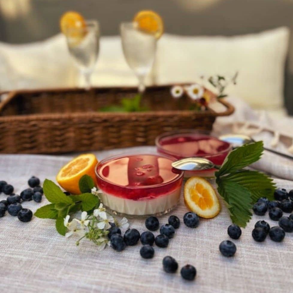 Desserts in glass bowls topped with red glaze, surrounded by blueberries, lemon, mint, and cocktails.