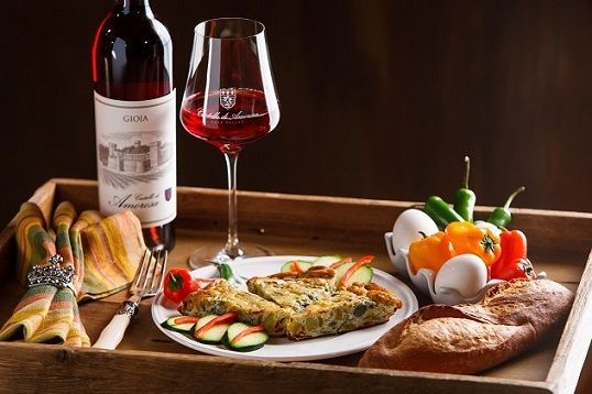 Wine bottle, glass, frittata, vegetables, and bread on table