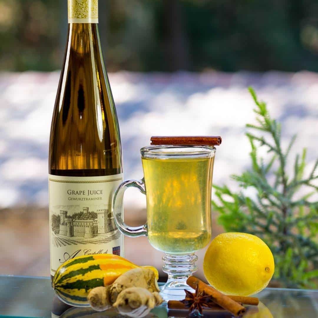Bottle of white wine, mug of hot wine with cinnamon stick, lemon, ginger, star anise, squash, and rosemary.