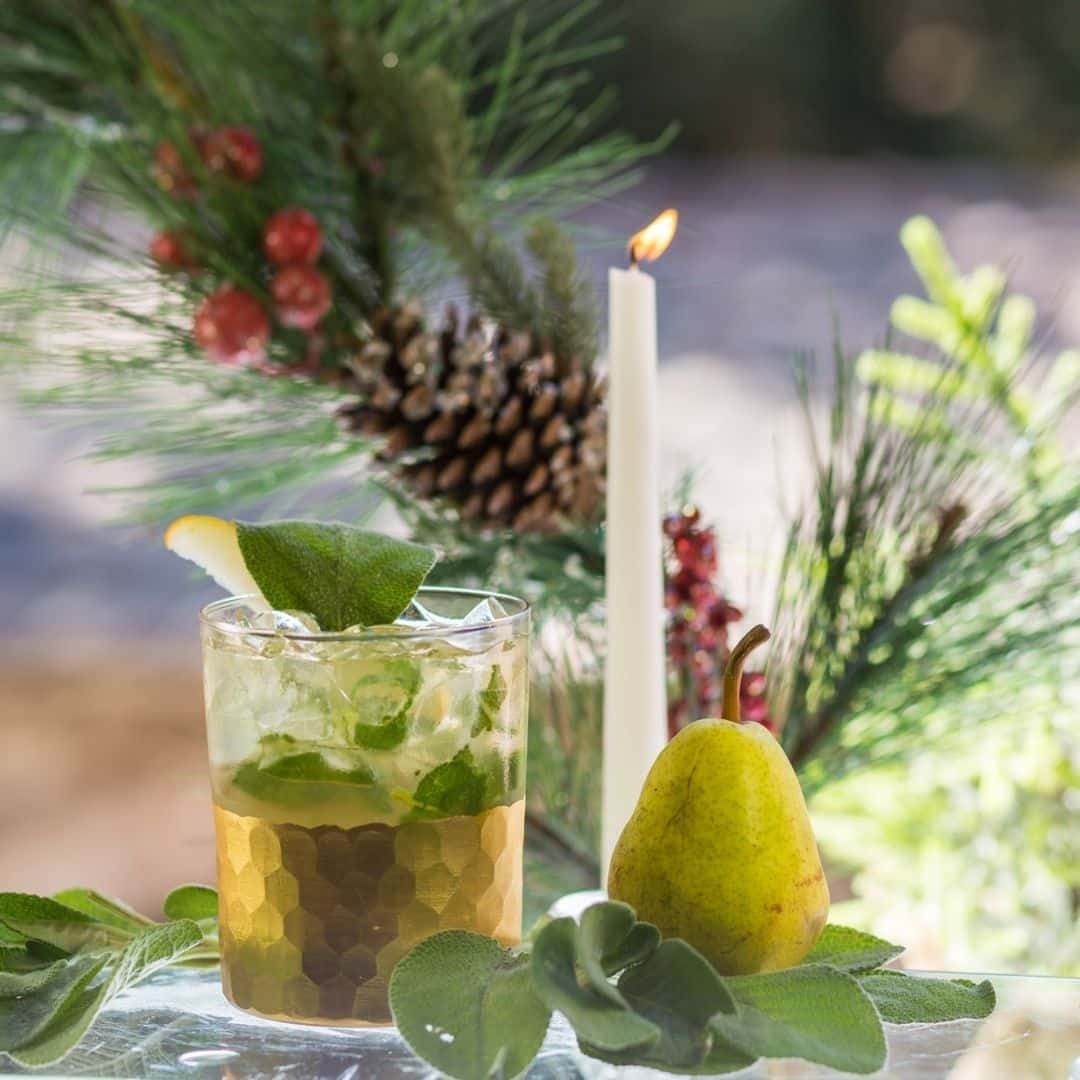 Cocktail in a glass with mint and a pear, decorated with a pine branch, candle, and berries.